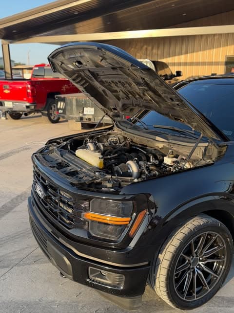 Black performance truck with its hood open inside Jorge's shop