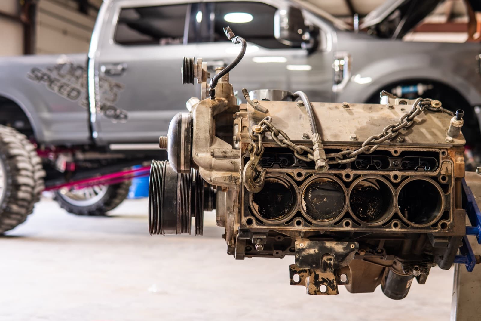 Engine block on a stand with a shop-lettered truck on the lift behind it