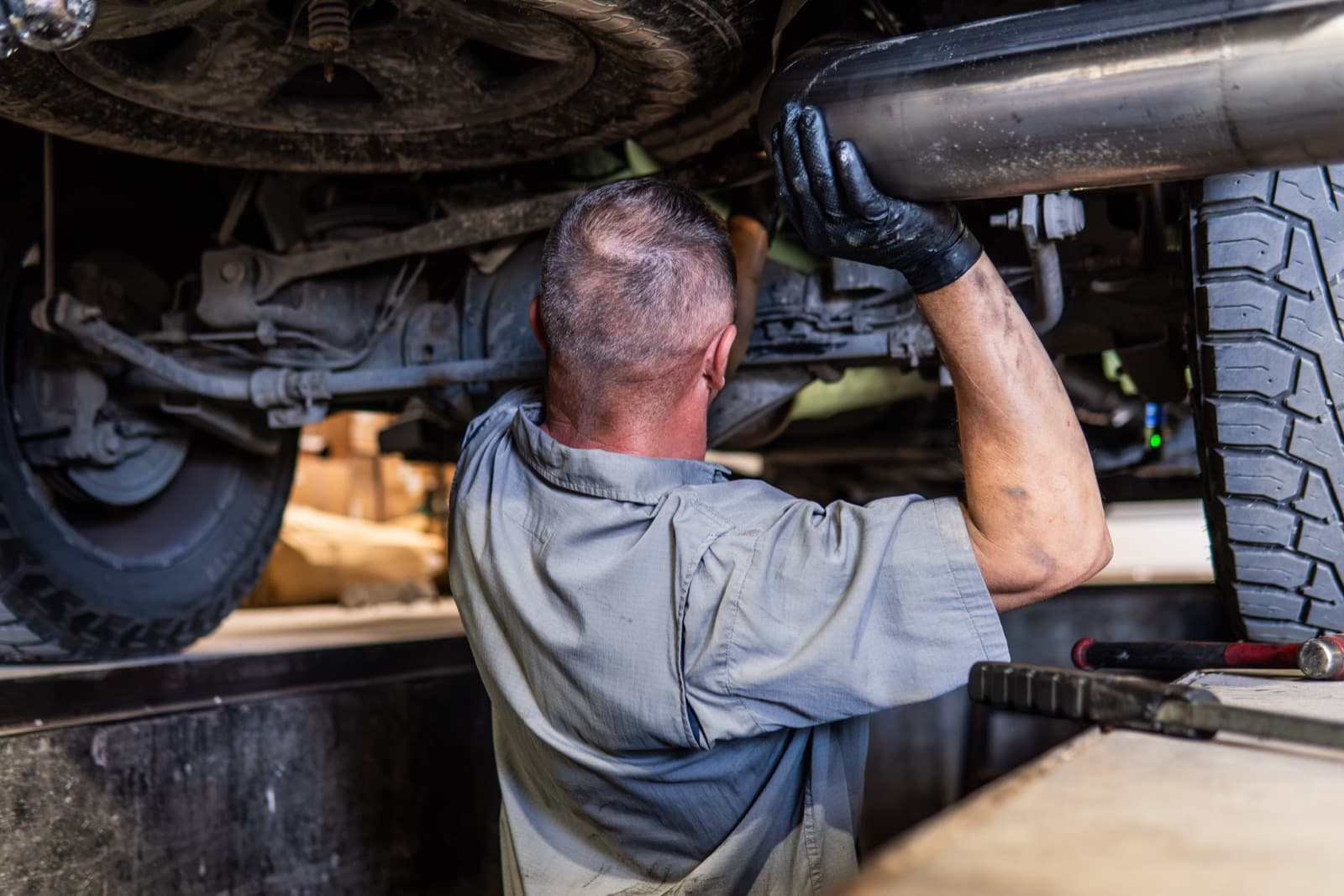 Technician fitting an exhaust section underneath a lifted truck